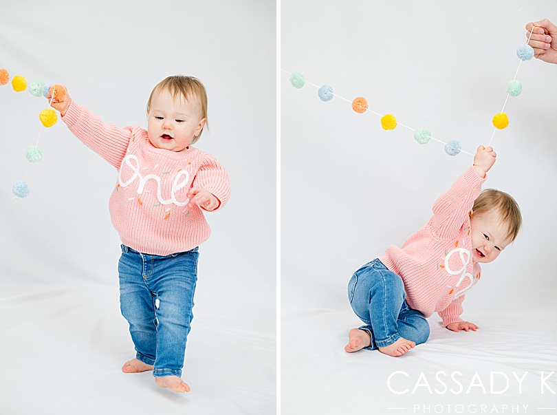 Baby standing up and holding pom poms in travel portrait studio session
