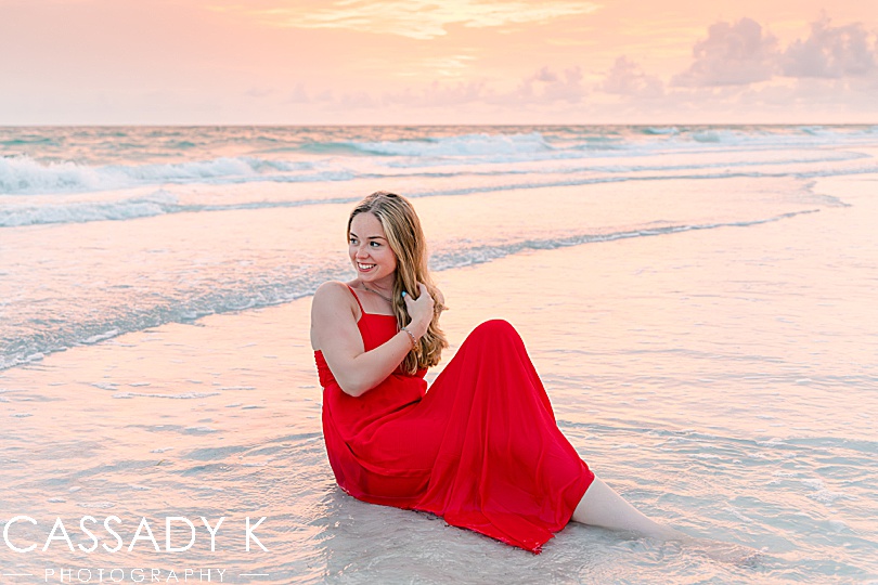 Girl in red dress sitting in ocean during Longboat Key Senior Portrait Session