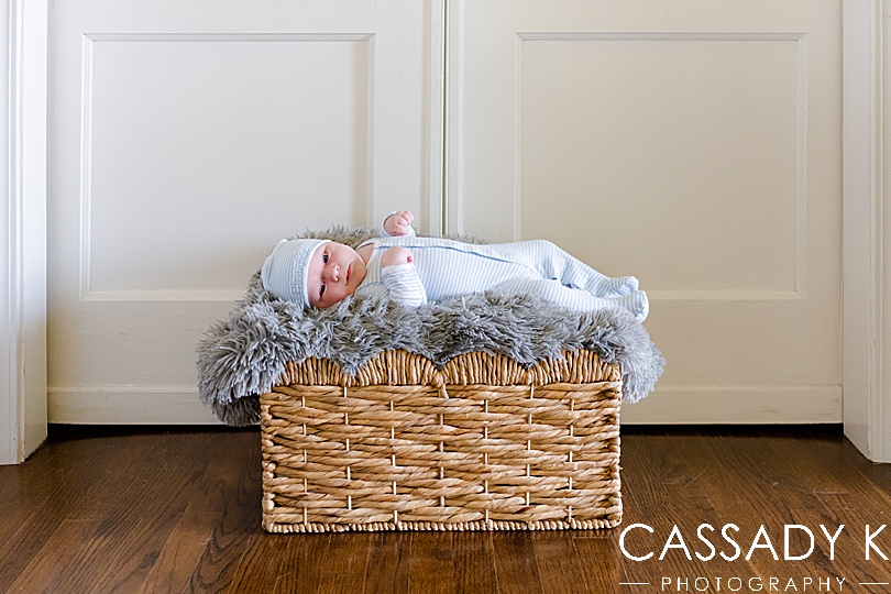 Baby boy in striped onesie laying in a basket during a growing family lifestyle session in Pittsburgh