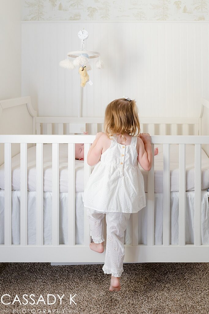 Sister looking into crib at newborn baby brother during Growing Family Lifestyle Session