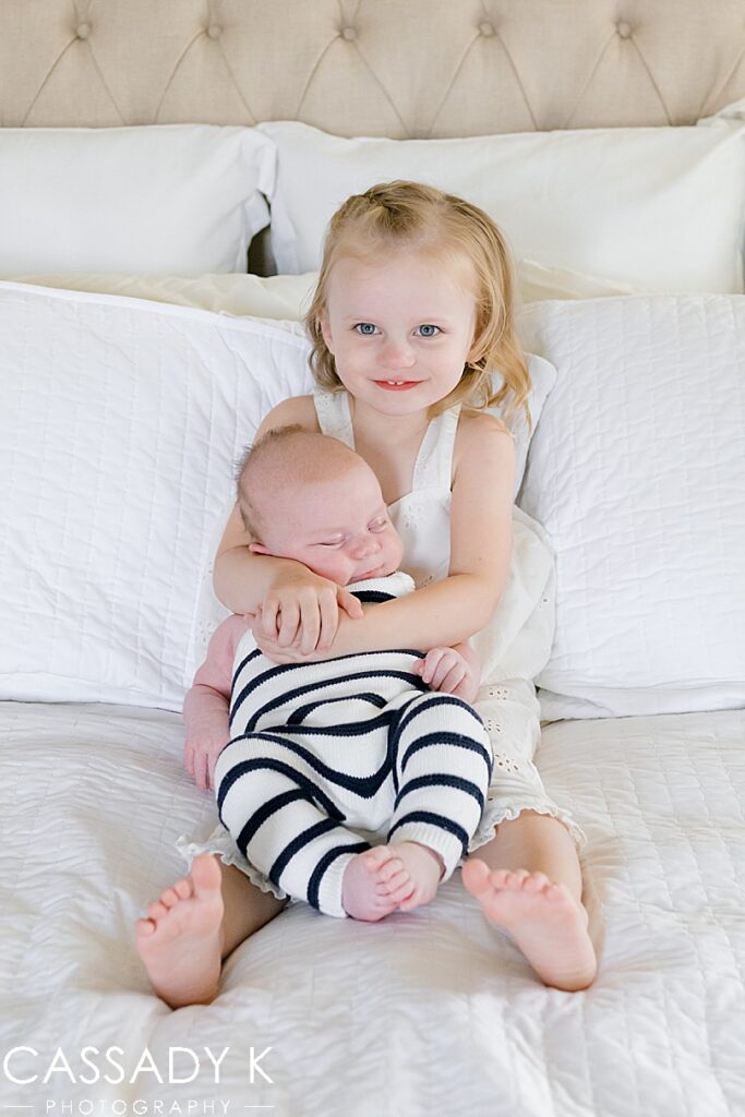 Young girl holding newborn baby brother in bed during Growing Family Lifestyle Session