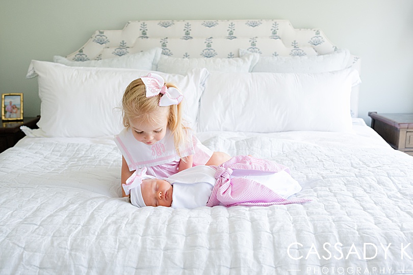 Big sister looks at little sister with matching monogrammed bows and outfits during a Doylestown family newborn session