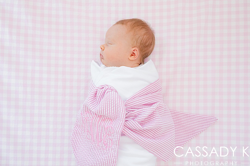Baby girl laid in her crib and wrapped in a white blanket and pink monogrammed bow during newborn session.