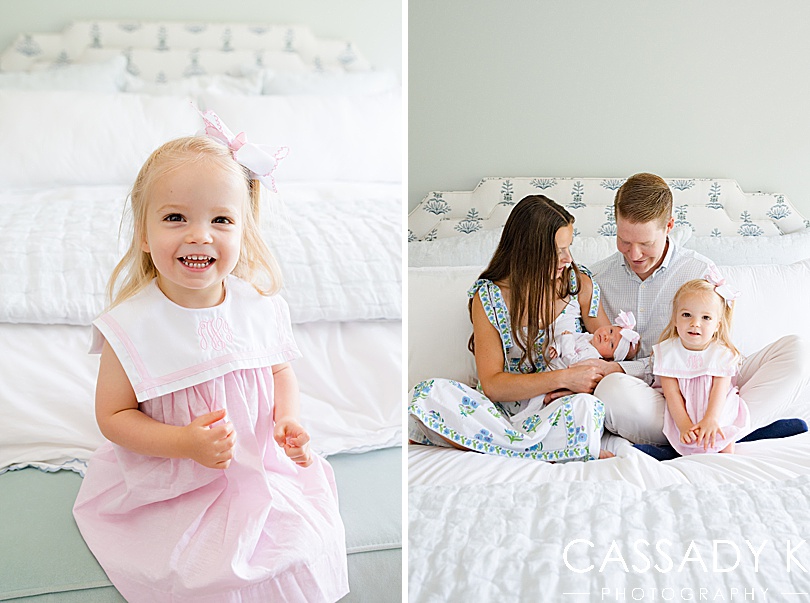 Older sister smiles big for her own picture during a family newborn session in Doylestown, PA. She's wearing a monogrammed bow and dress in pink.